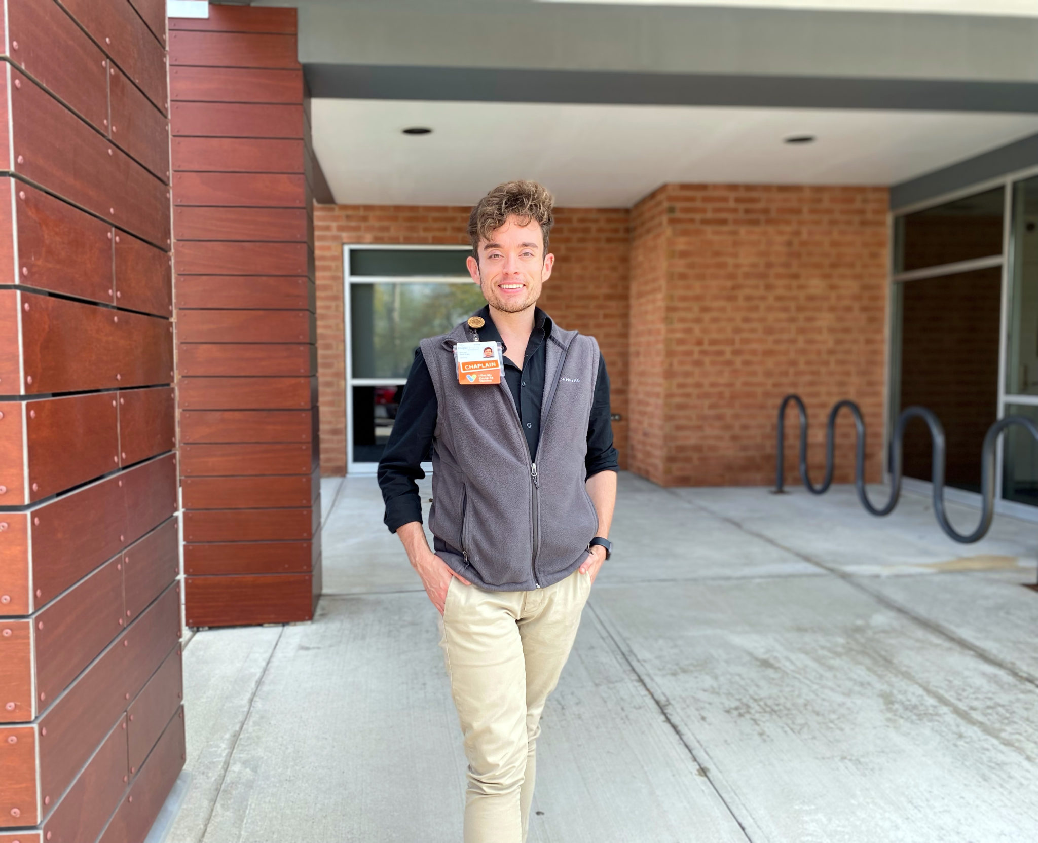 Young man in gray vest standing outside entrance to building