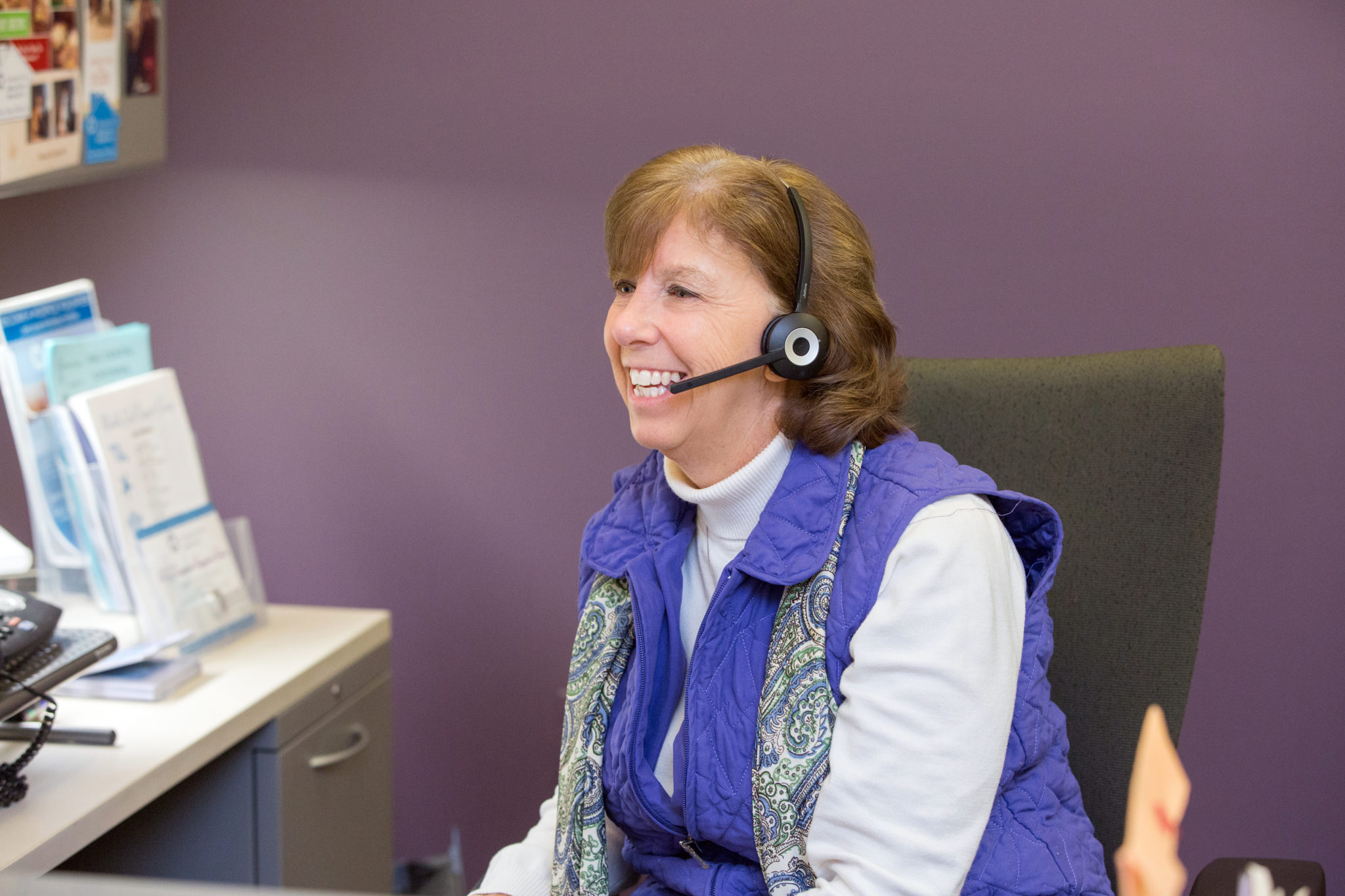 head and torso of woman at computer wearing headset with a purple wall