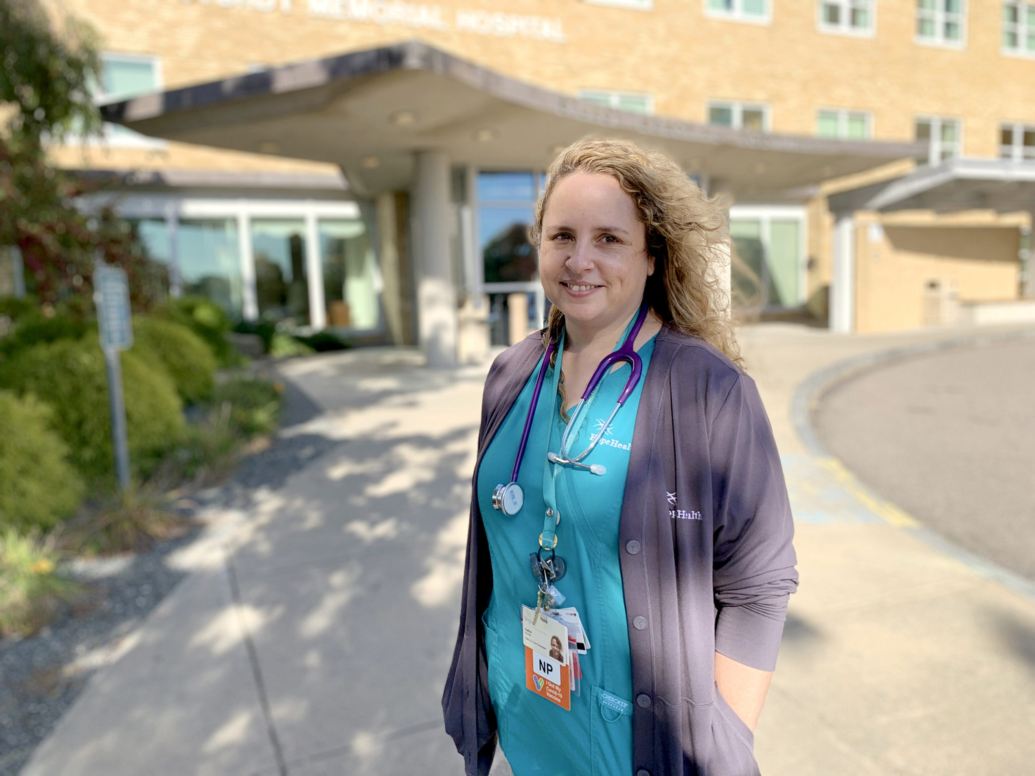 Woman in hospital scrubs stands uotside hospital entrance