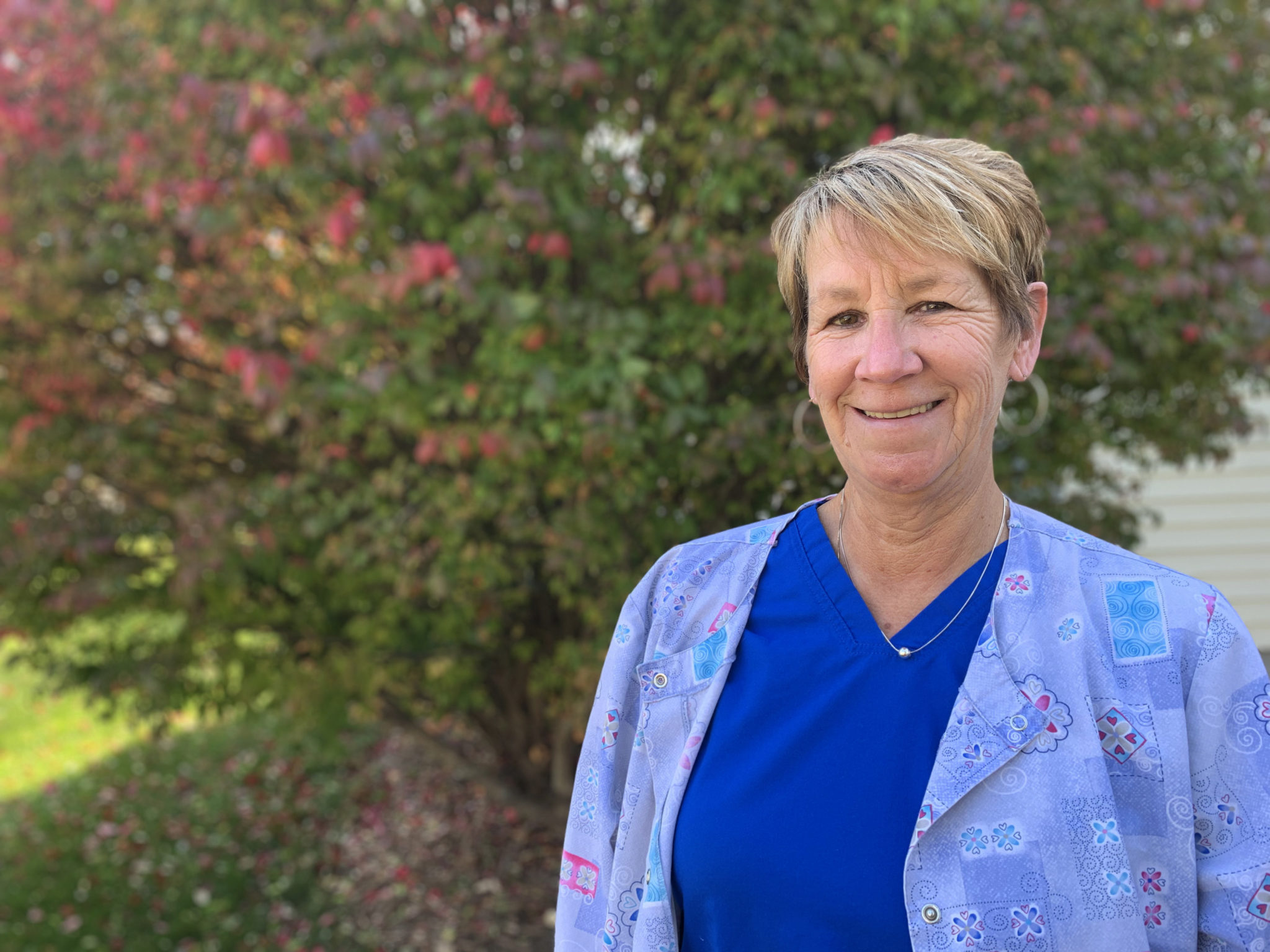 woman in blue scrubs and smock stands in yard