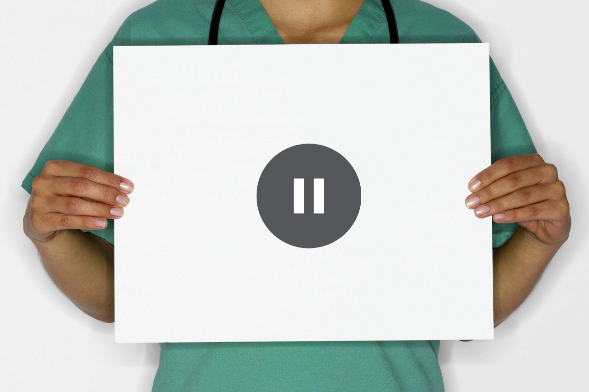 person in scrubs holding sign with pause symbol