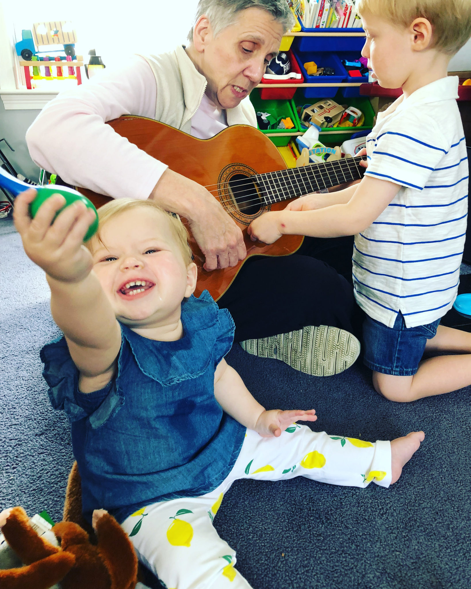 baby smiles and toddler is interested in guitar played by older woman