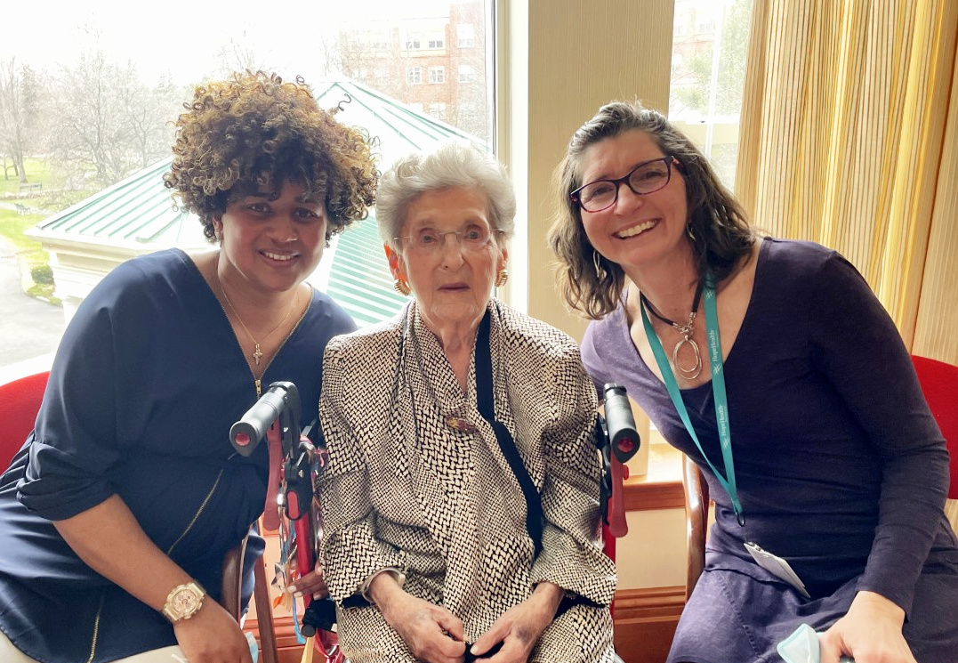 Two young women sit on either side of an elderly woman. The woman on the right is a volunteer who helped the elderly woman finish a legacy project of completing a book