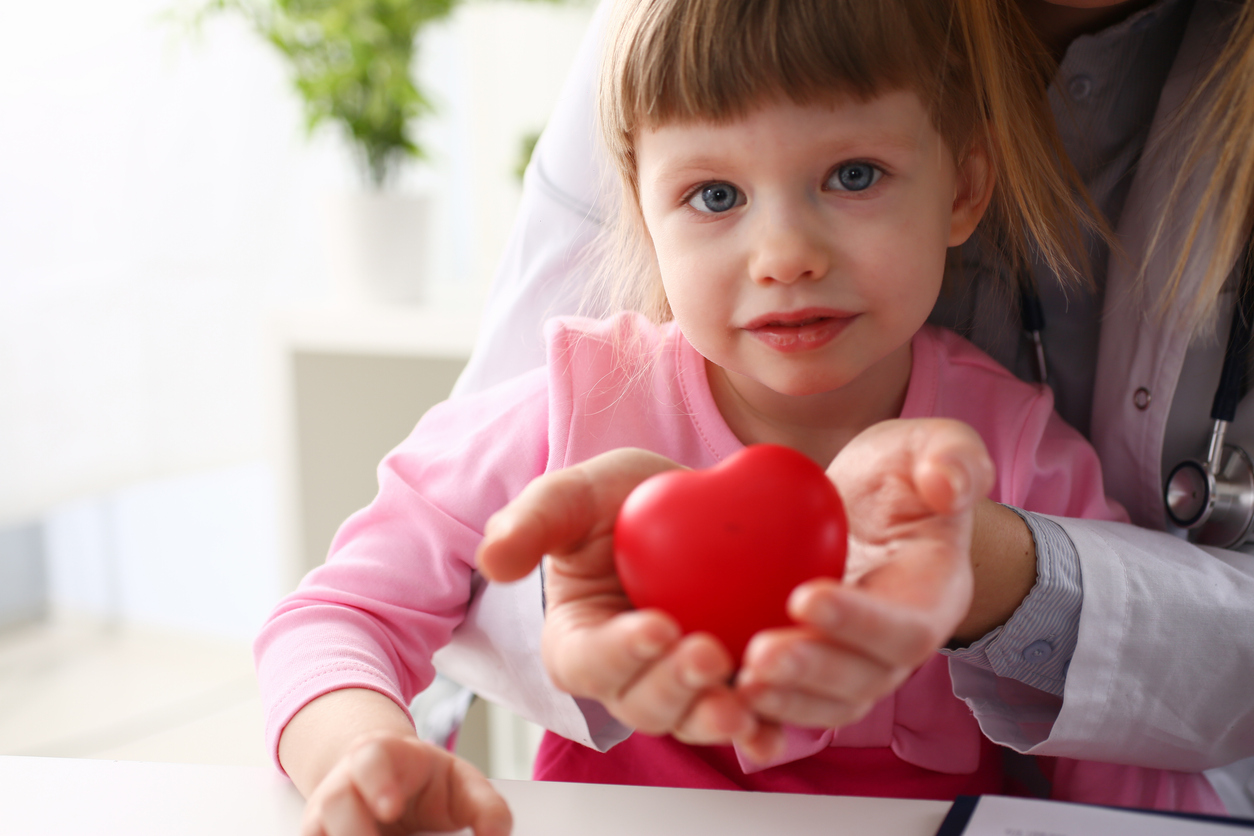 Little baby girl visiting doctor holding in hands red toy heart as life safe symbol