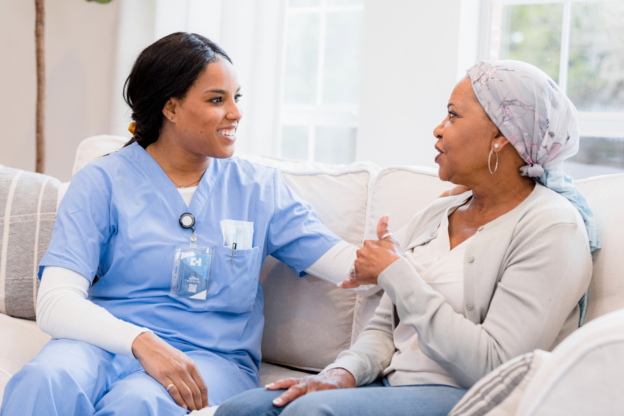 The nurse sits with her patient on the couch and have good conversation.