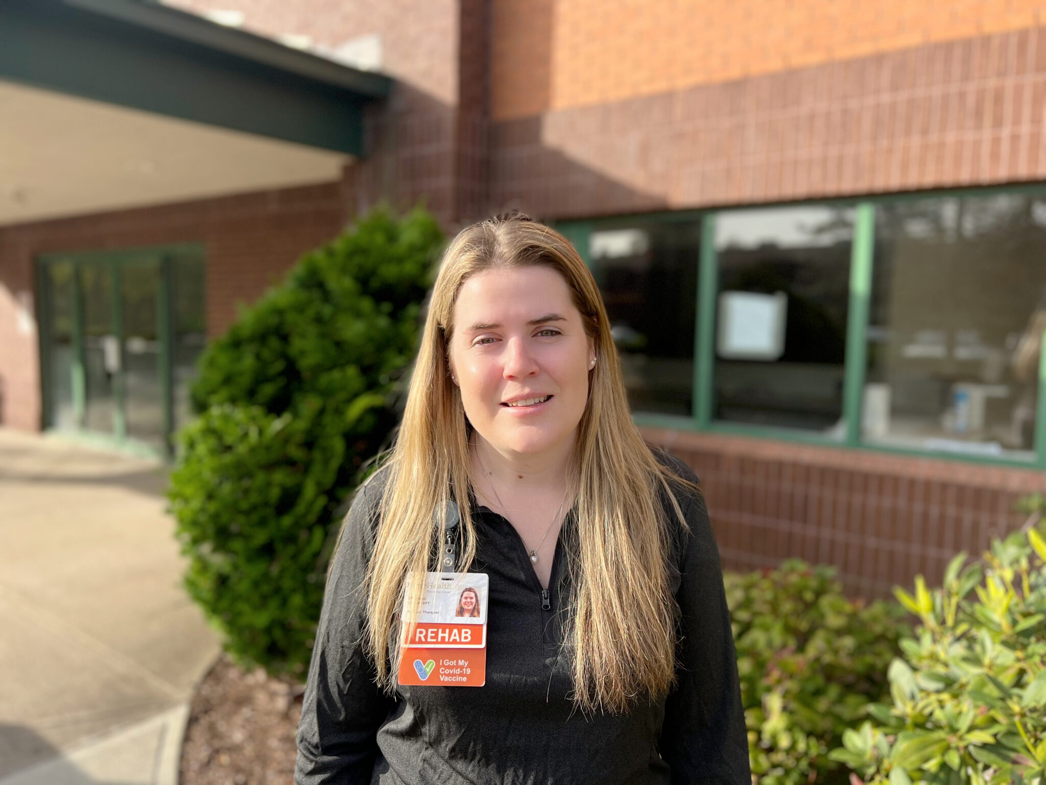 Photo of a physical therapist standing in front of a brick building