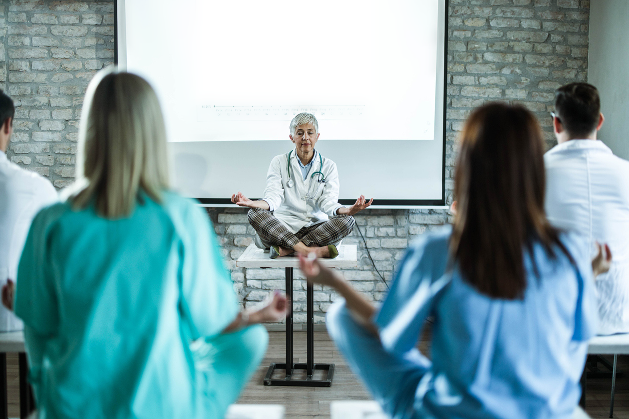 Mature female doctor leading Yoga class in a board room.