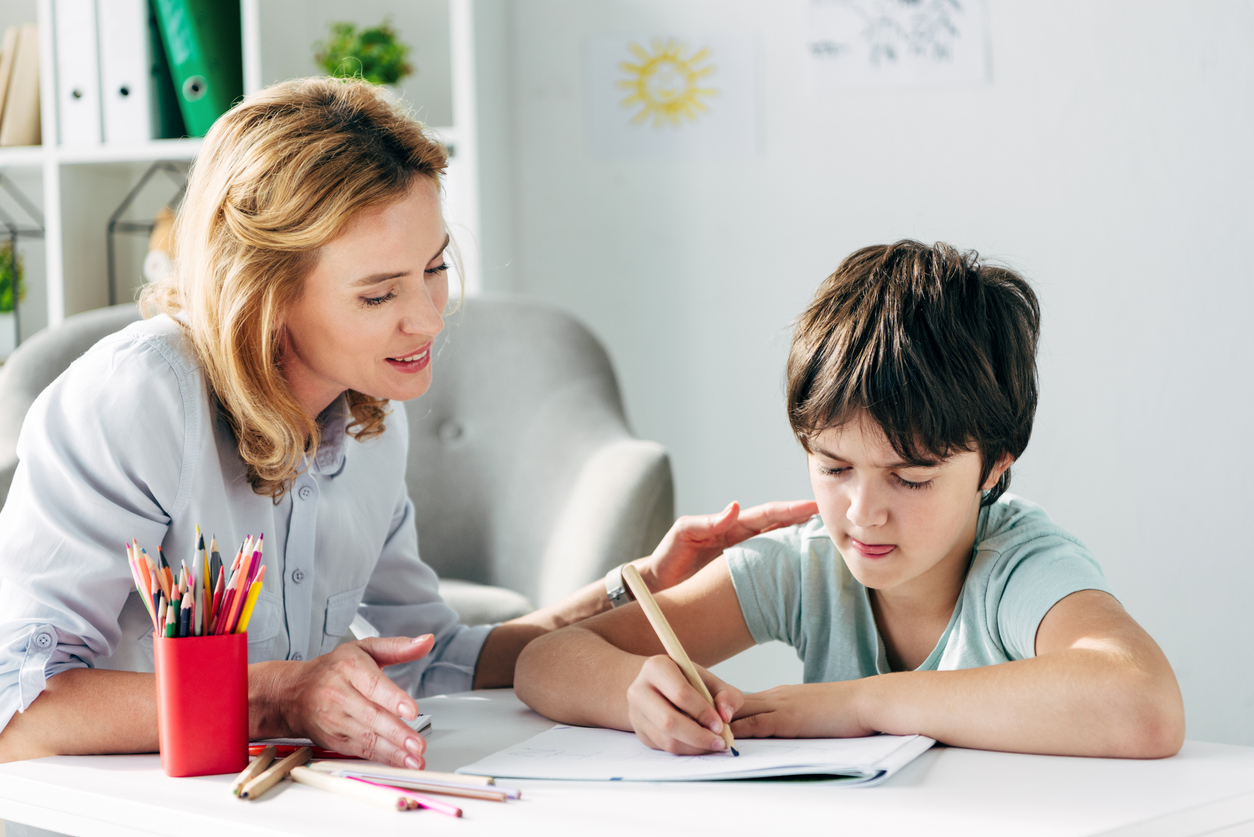 kid with dyslexia drawing with pencil and child psychologist looking at it