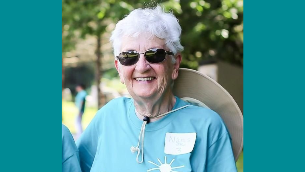 Elderly woman with white hair wearing sunglasses and a hat around her neck