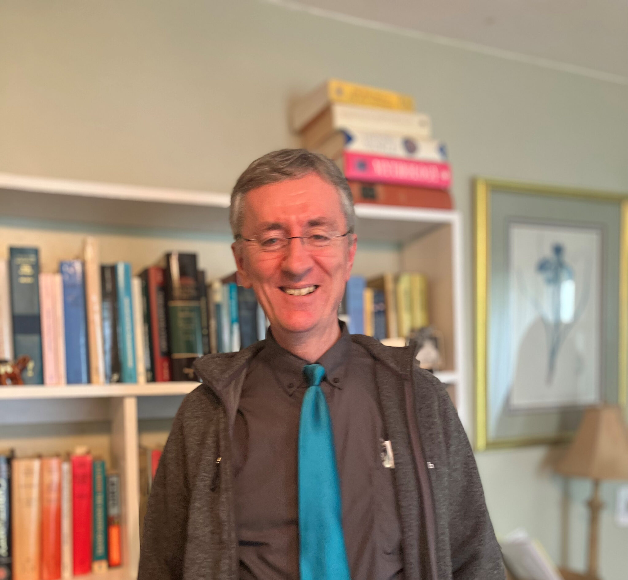 Man wearing teal tie standing in front of a bookshelf