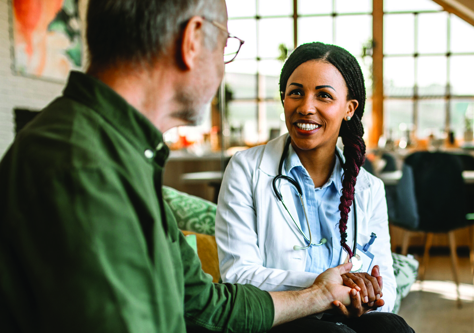 Female mid adult doctor at home visit comforting patient, holding his hand