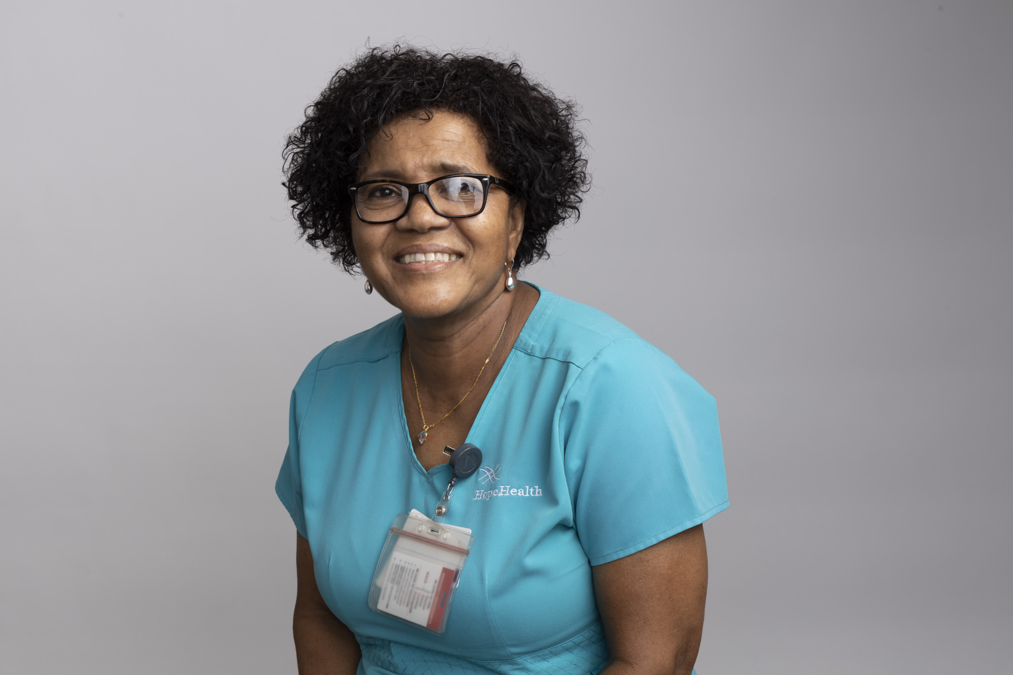 Female hospice aide wearing glasses in her teal scrubs smiling warmly