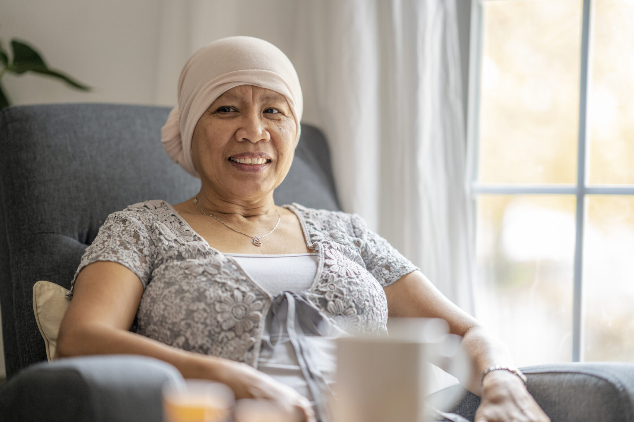 Elderly Filipino woman diagnosed with cancer sitting in her home with a headscarf.