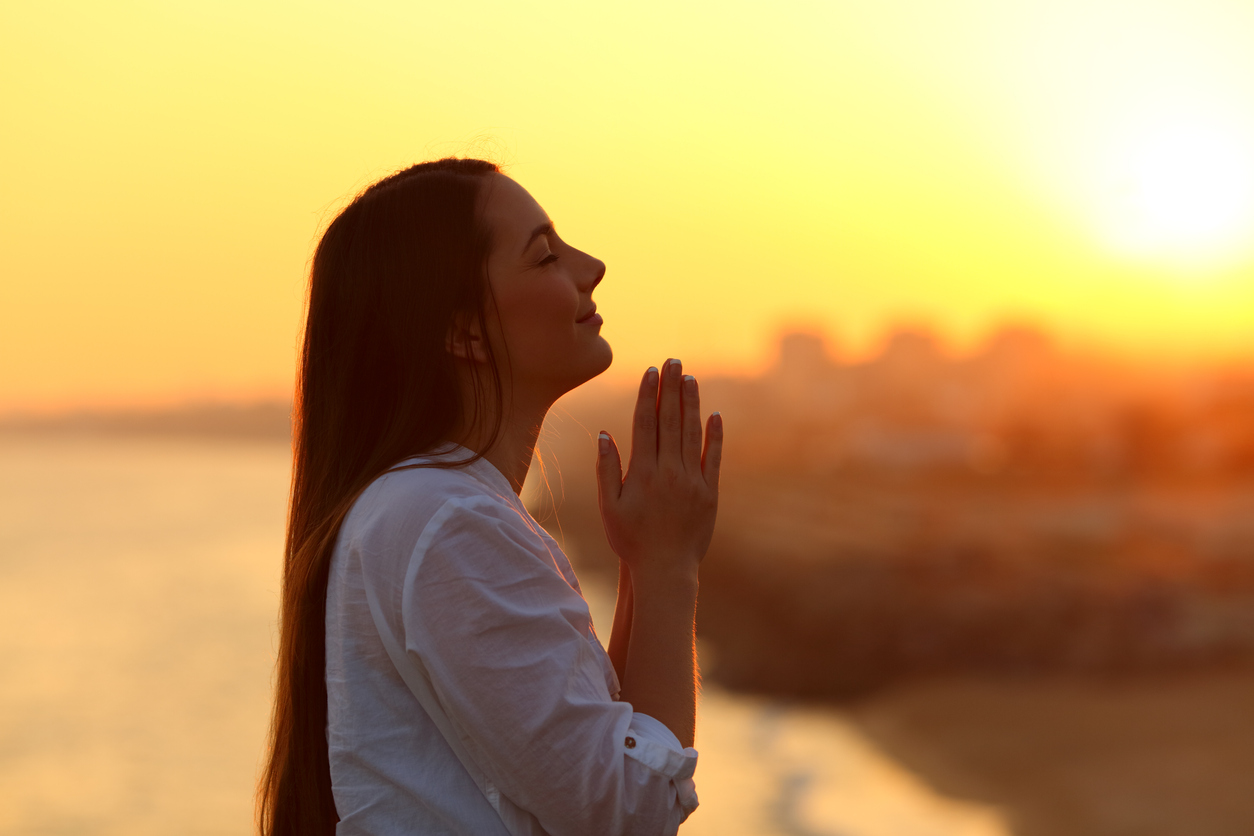 Side view backlight portrait of a grateful woman praying and looking above at sunset