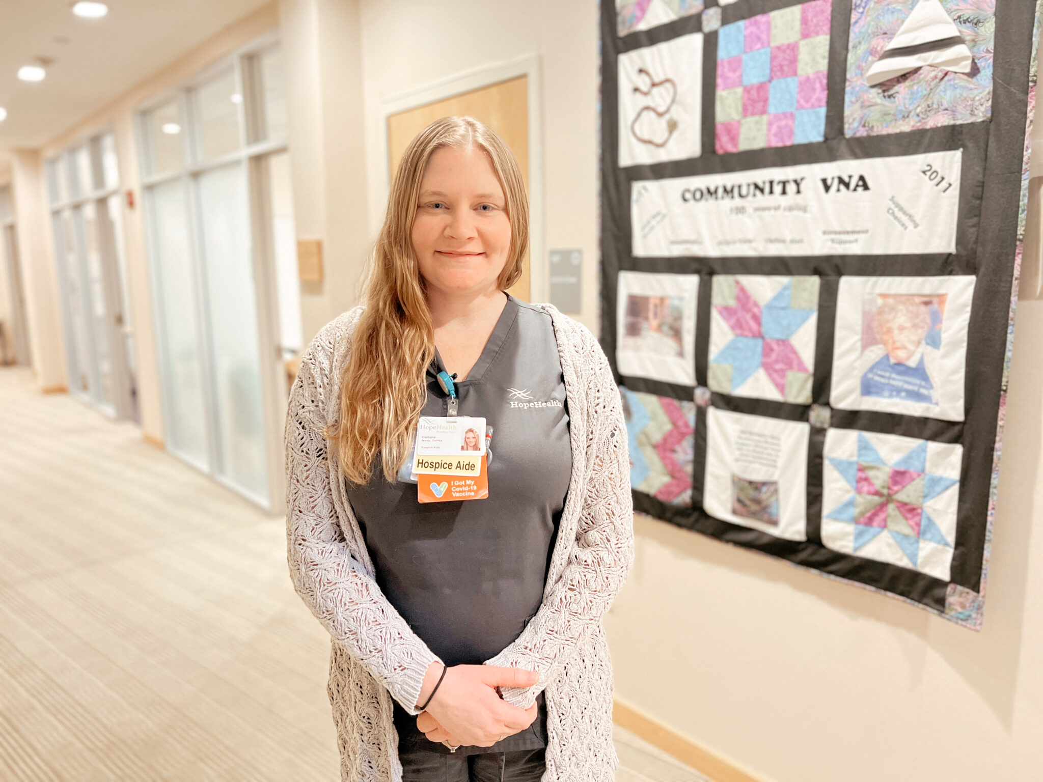 Female hospice aide smiling in front of a commemorative quilt