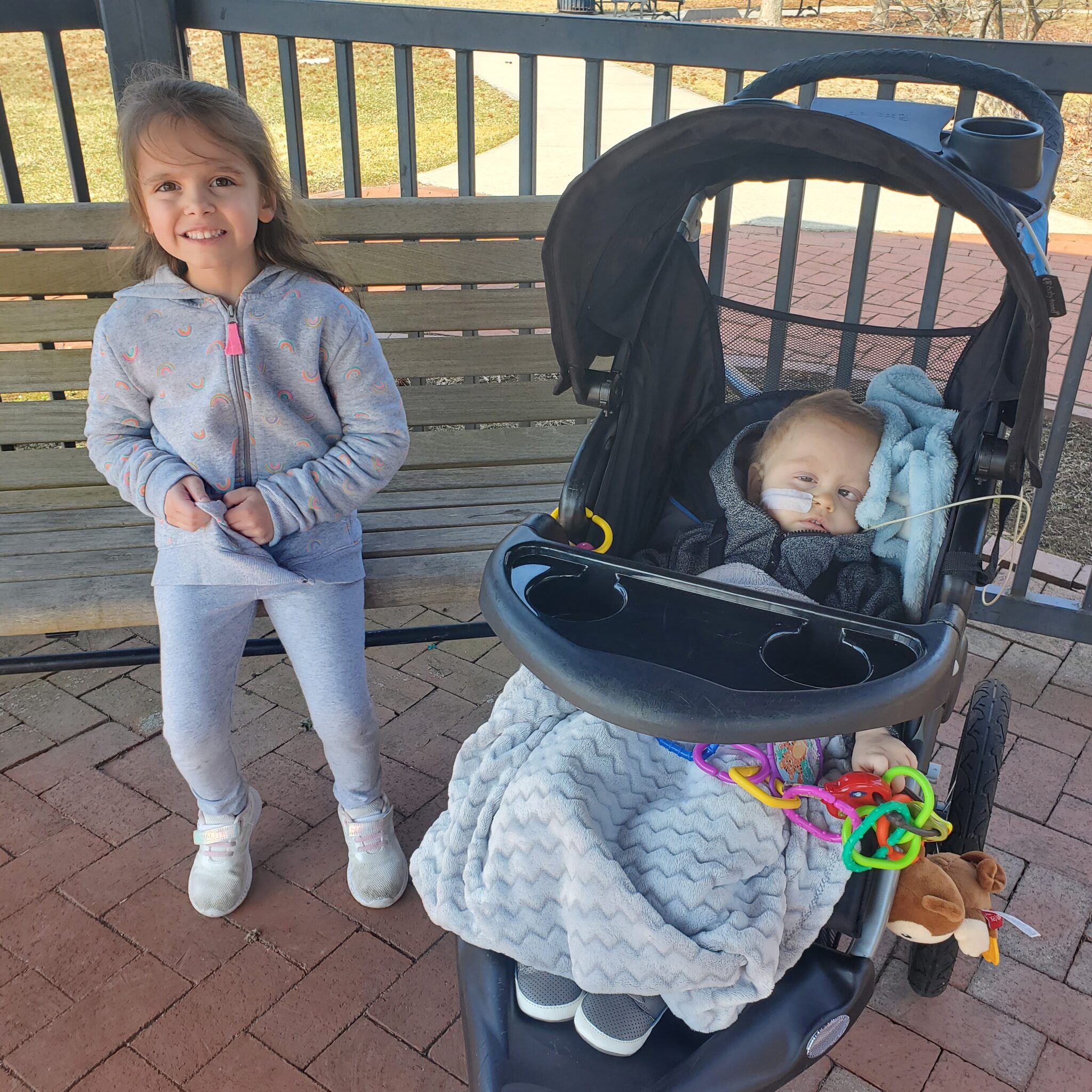 Sister posing for a photo next to her baby brother in a black stroller
