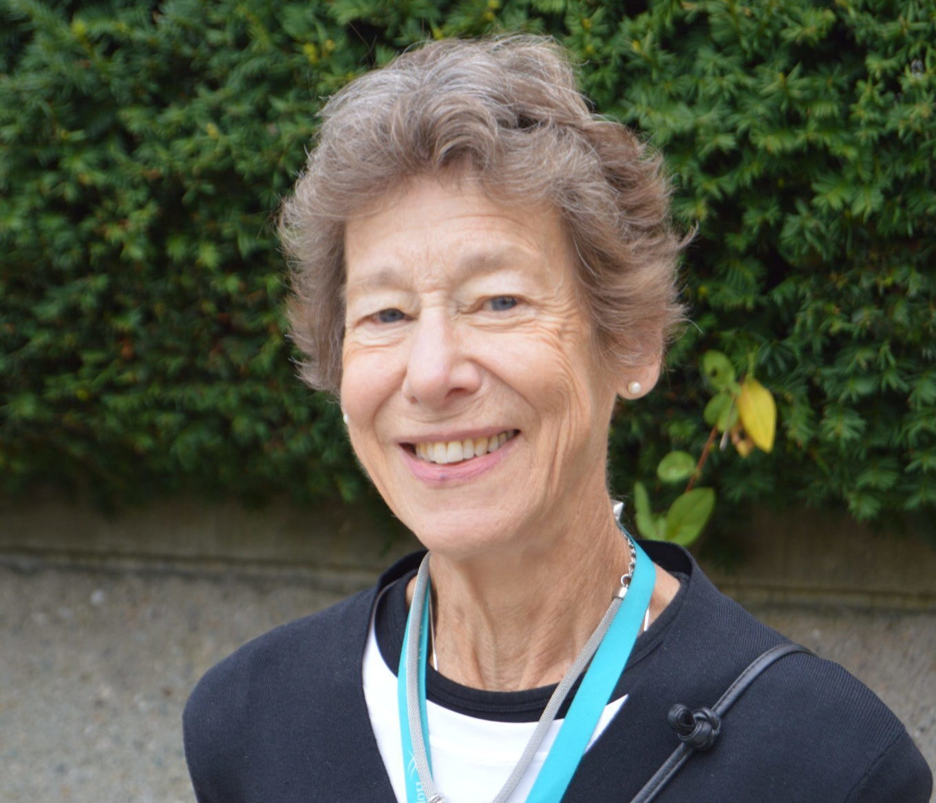 Woman with short hair and black shirt smiling in front of greenery