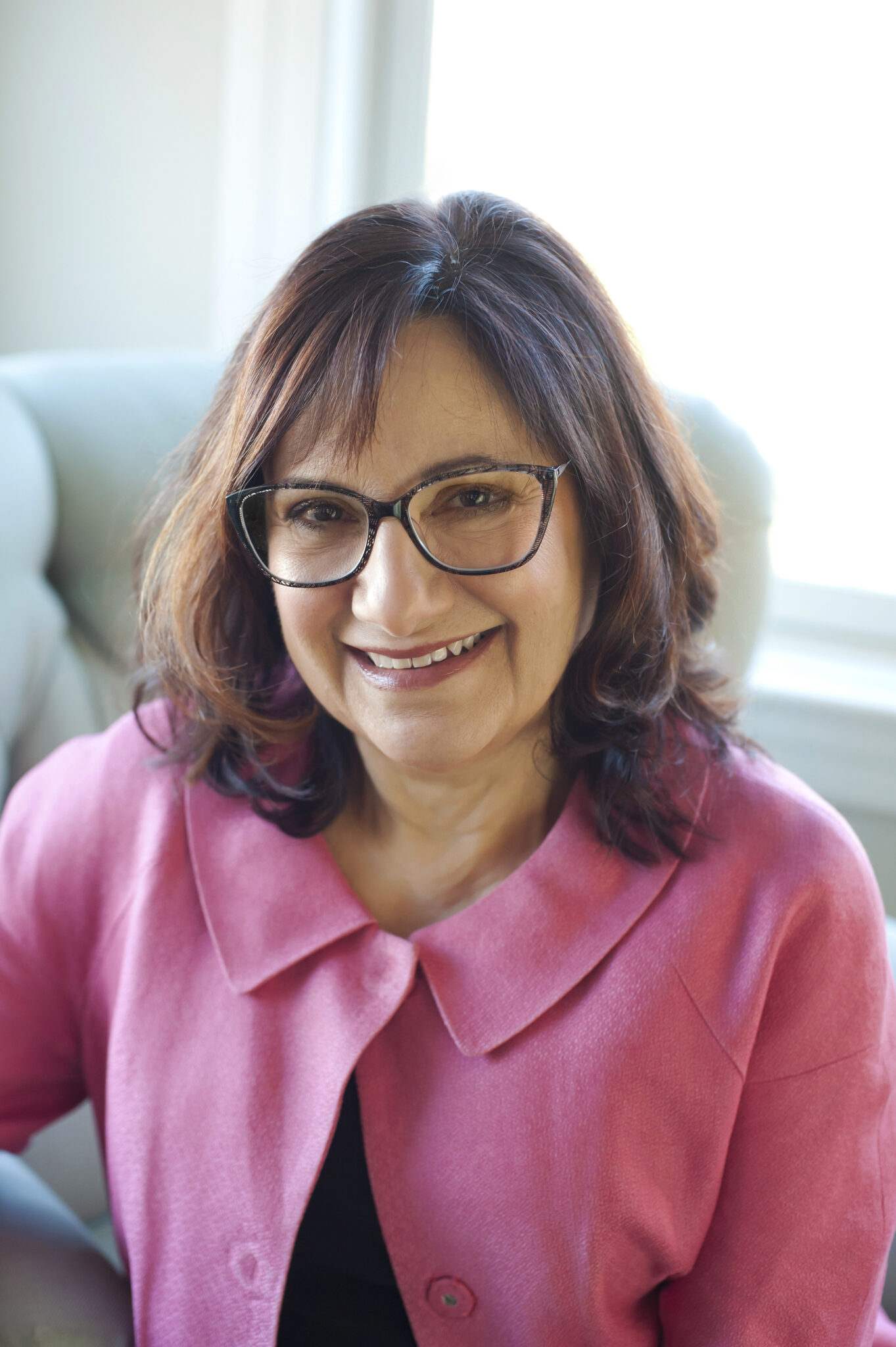 Woman in pink blazer and glasses smiling in a well lit room