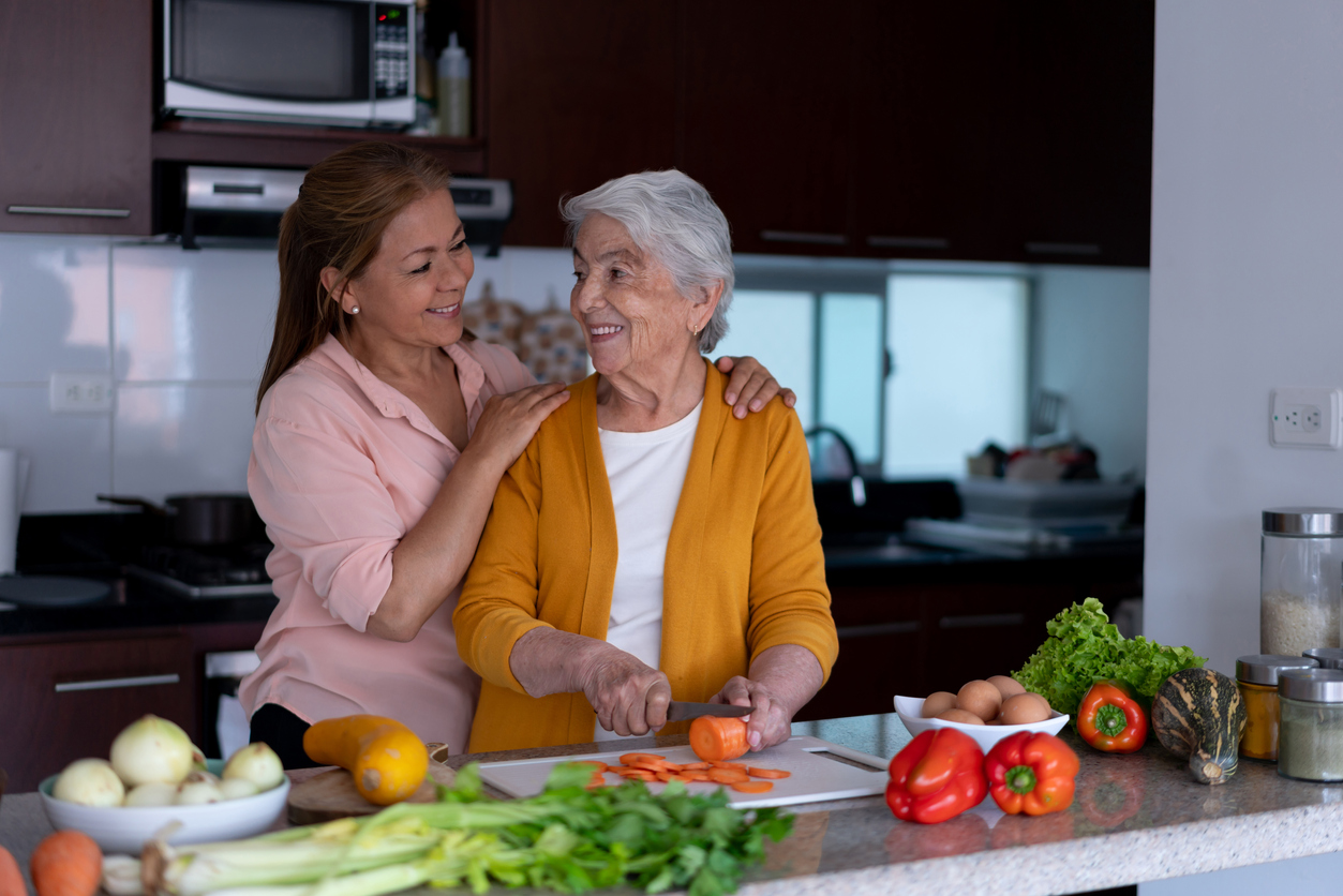 Sweet daughter and mother looking at each other lovingly while preparing a meal together at home - Lifestyles