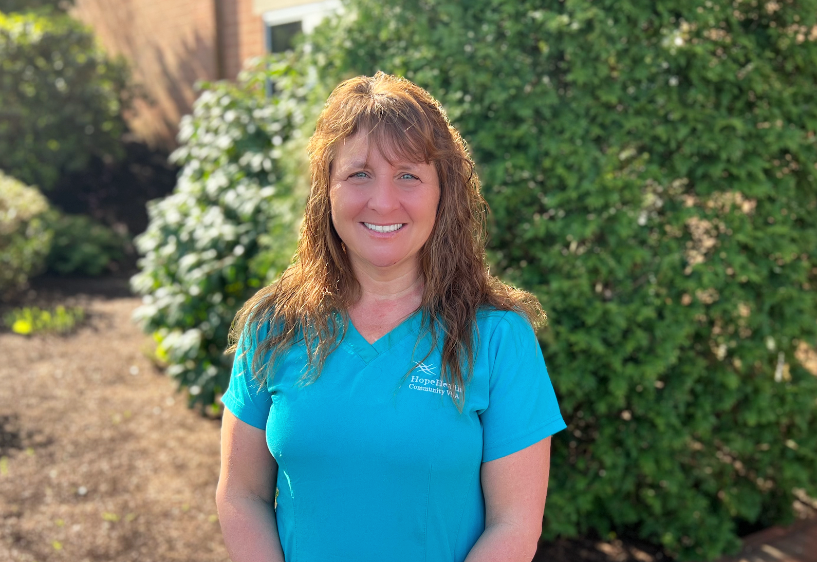 Occupational therapist in teal scrubs standing in a garden surrounded by greenery