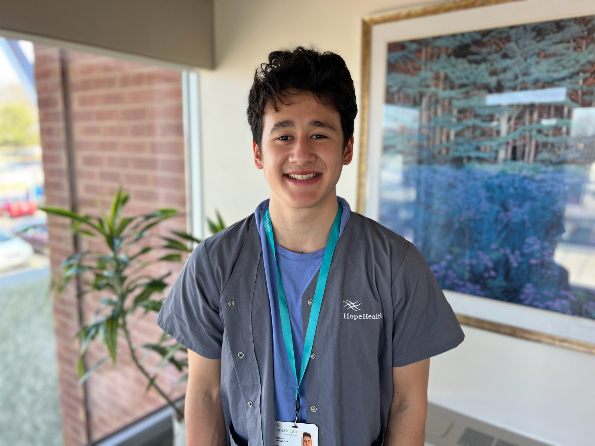 Young volunteer smiling in room with plant and painting behind him