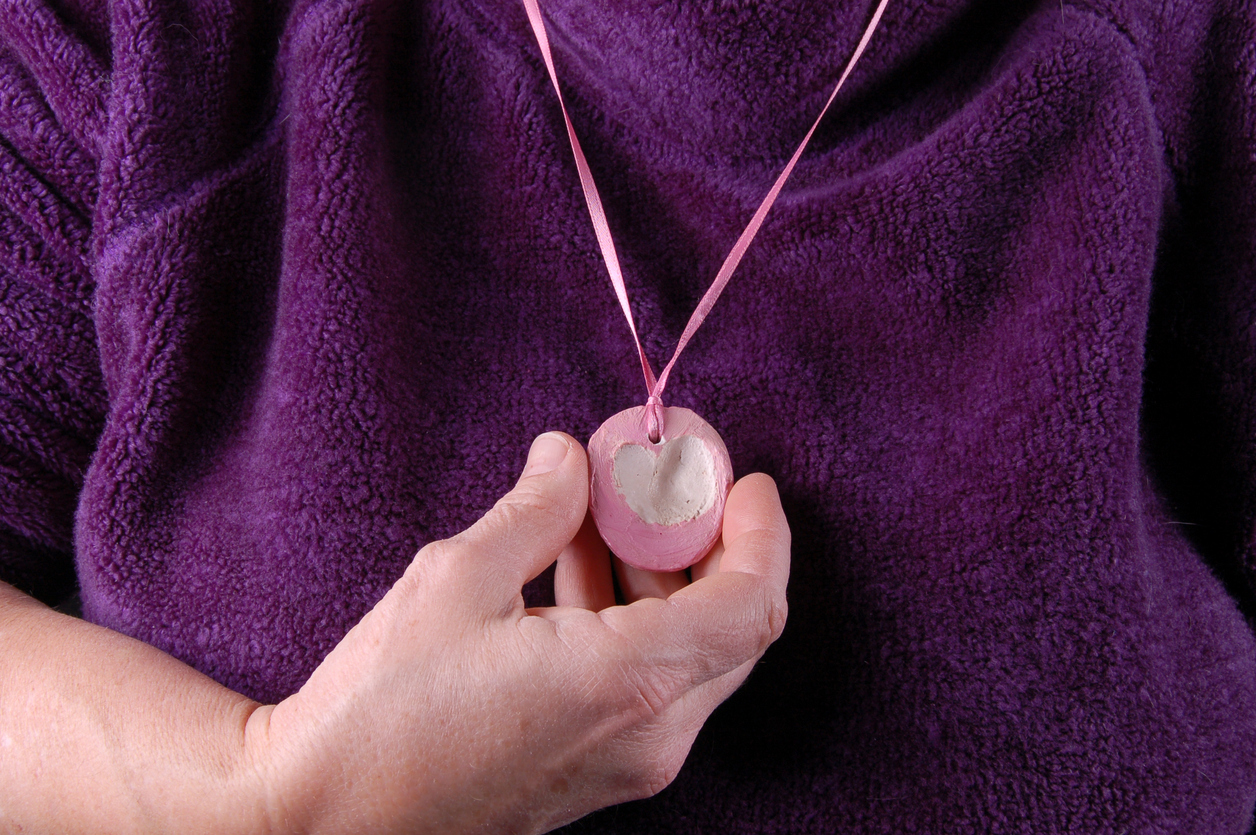 The rough hand of a mother holds the necklace her child made for her. The heart in the necklace was made from two thumbprints. The child is now grown up.