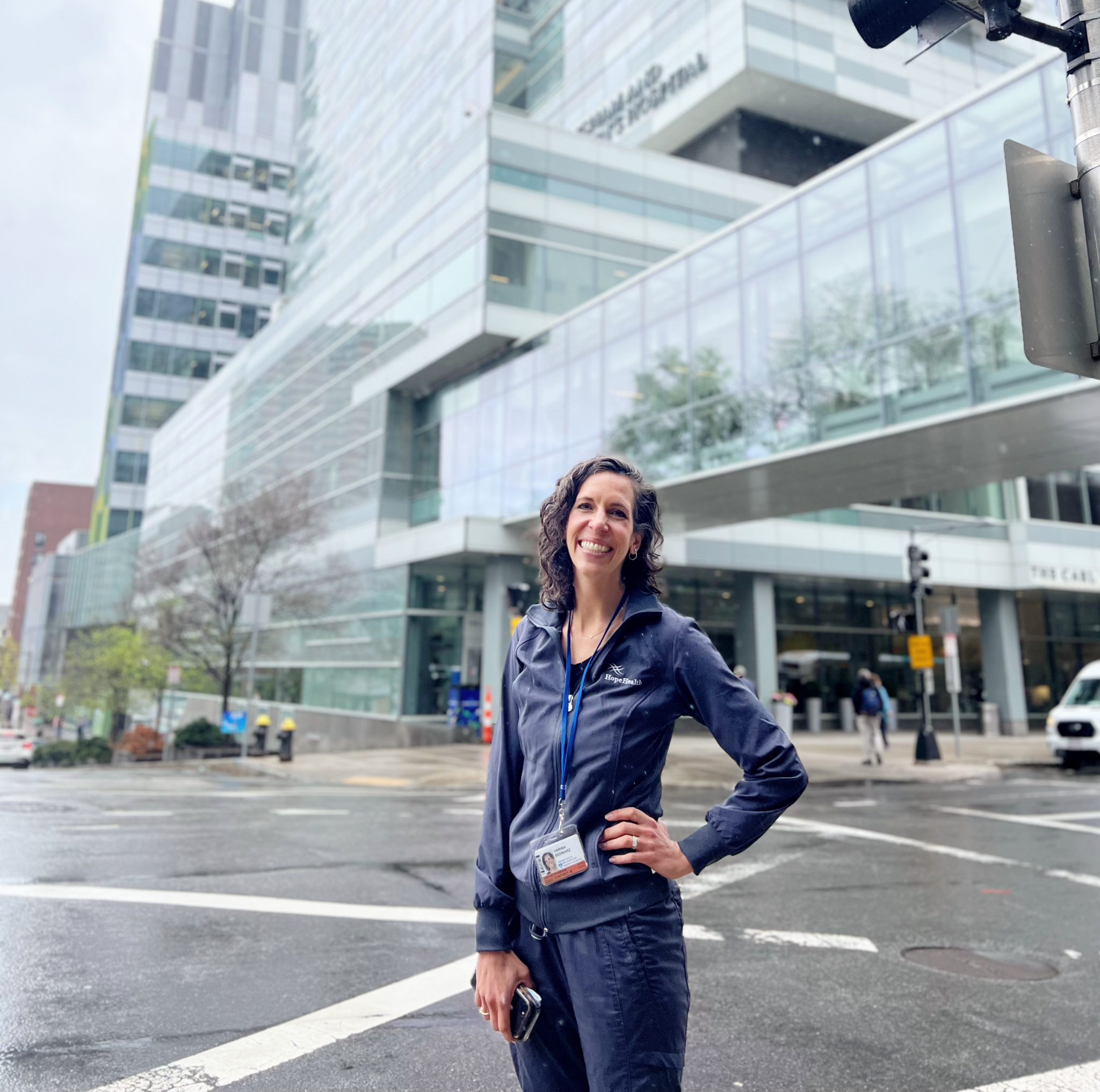 Nurse in grey scrubs stands in front of tall glass buildings