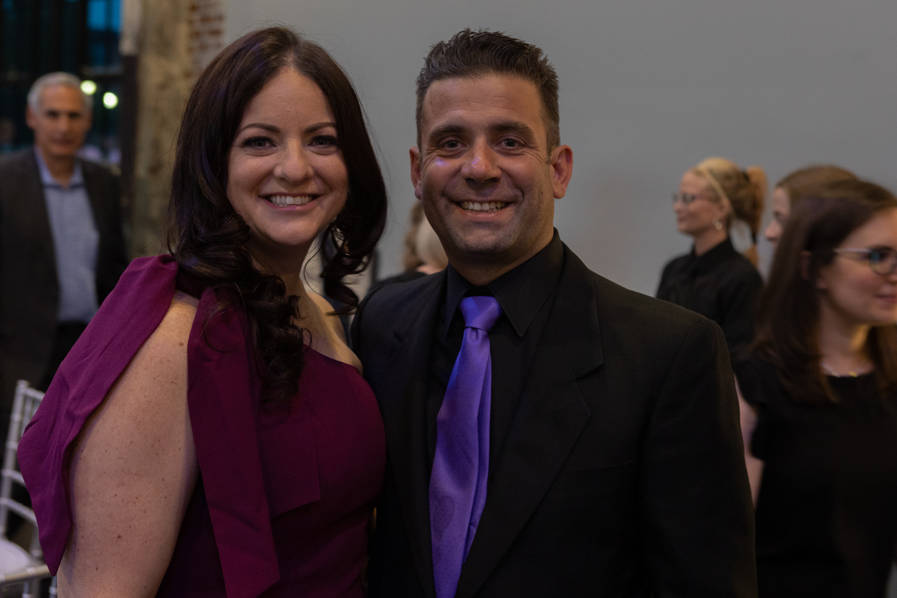 Woman in purple dress posing next to a man wearing a black suit and purple tie