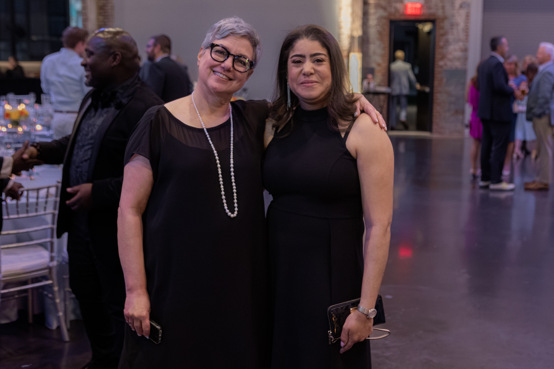 Two women in black dresses smiling in an event venue