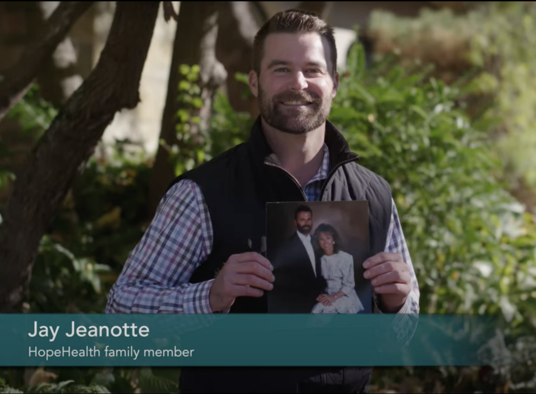 Photo of a man holding up a photo of his parents