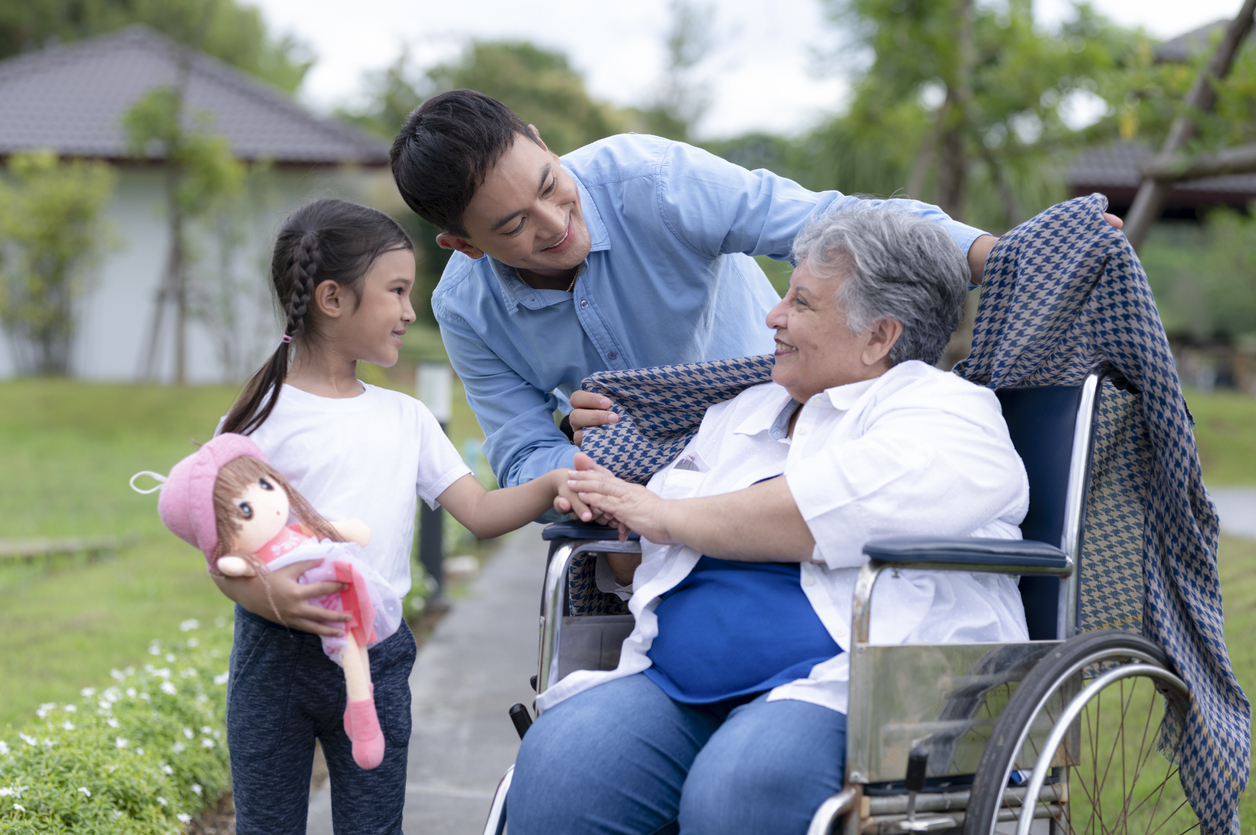 Asian young man and woman caring for an elderly woman in a wheelchair at a nursing home, a winter-sleeve son warms a middle Eastern mother, a nursing care.