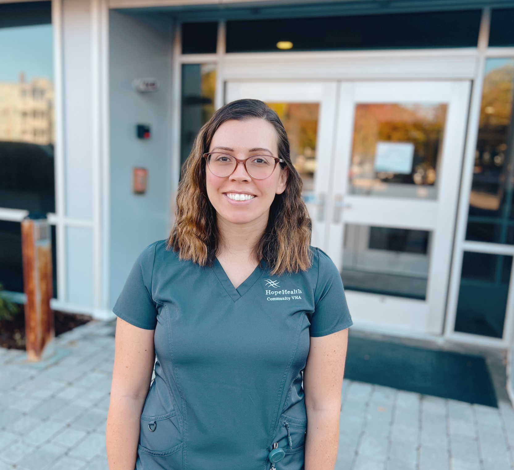 Physical therapist in gray scrubs stands in front of a building