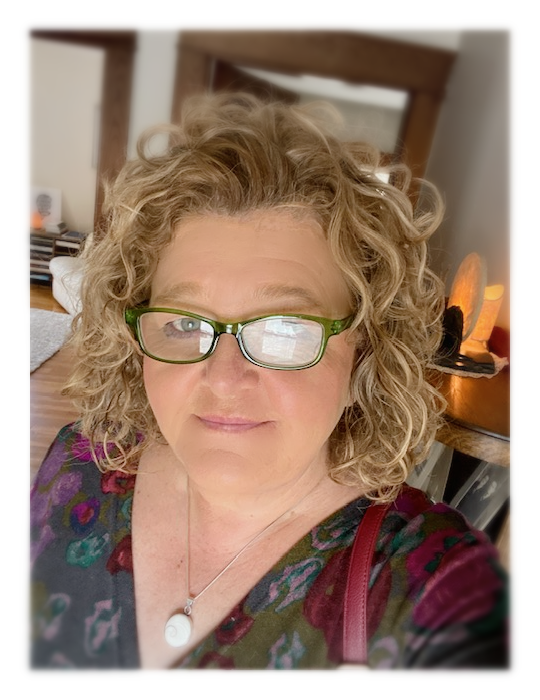 Blonde woman with curly hair and glasses smiles in a dimly lit room