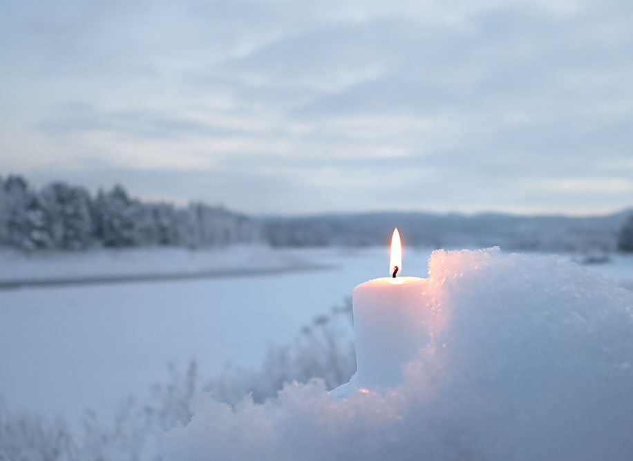 Holiday image with a candle in the white snow next to an ice-covered river. We see Finland from Sweden (Arctic Circle, Napapiiri)