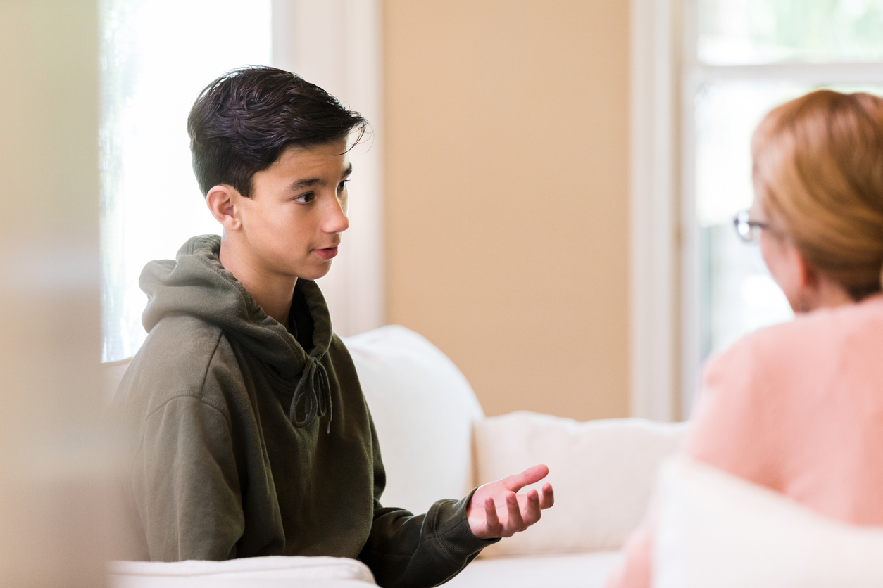 Young preteen boy in a green sweatshirt chats about serious illness and thoughts and concerns about end of life with his mom