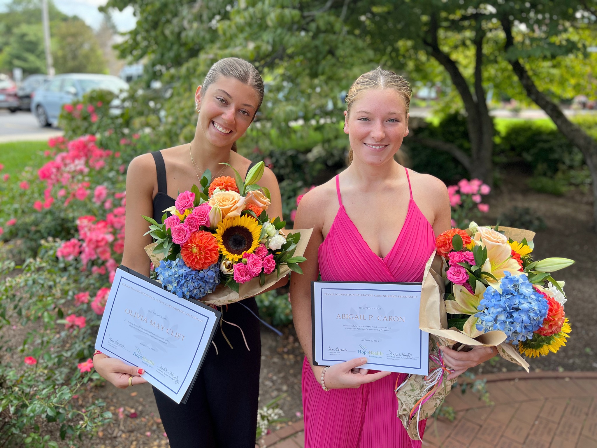 two young women holding a bouquet of flowers in a garden, graduating from their palliative fellowship with HopeHealth