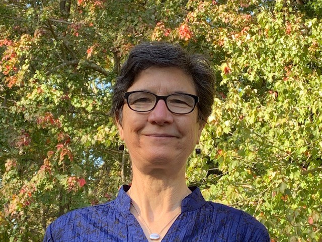 Woman with short hair wearing black rimmed glasses in front of green foliage