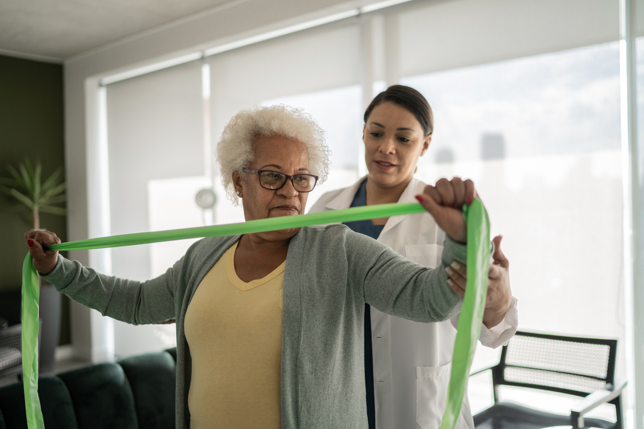 Physical therapist helping senior woman doing exercises with resistance band at home