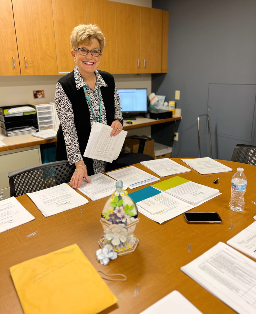 Woman with short blonde hair stands at desk organizing papers