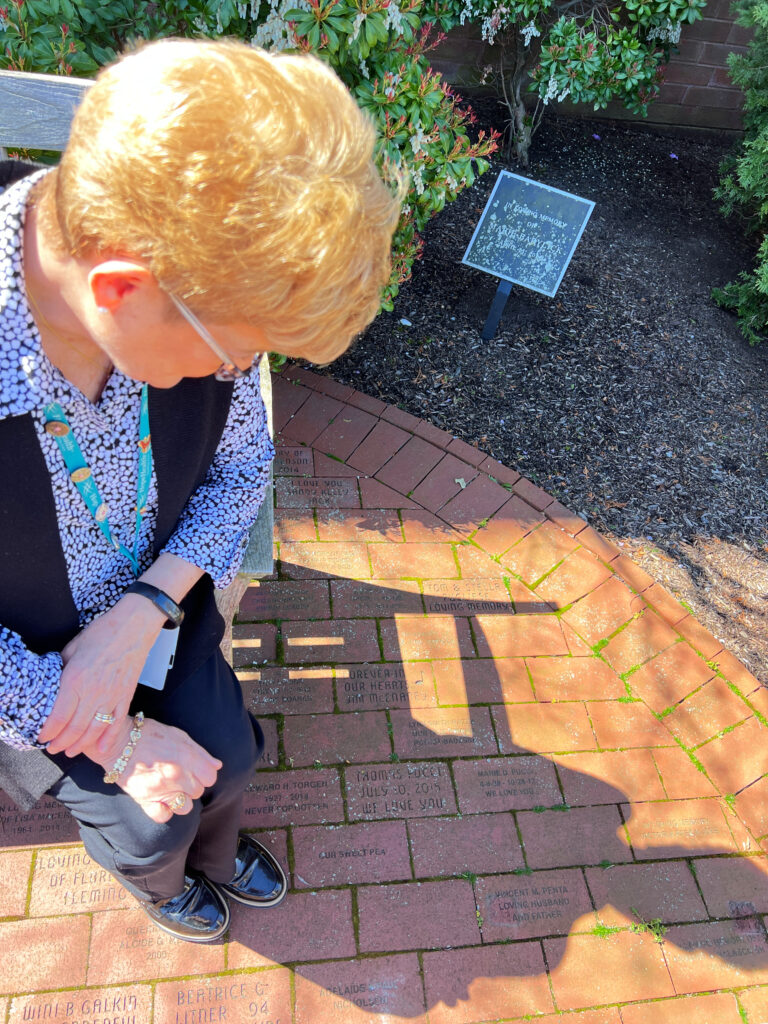 Woman with short blonde hair looks down at brick remembrance garden
