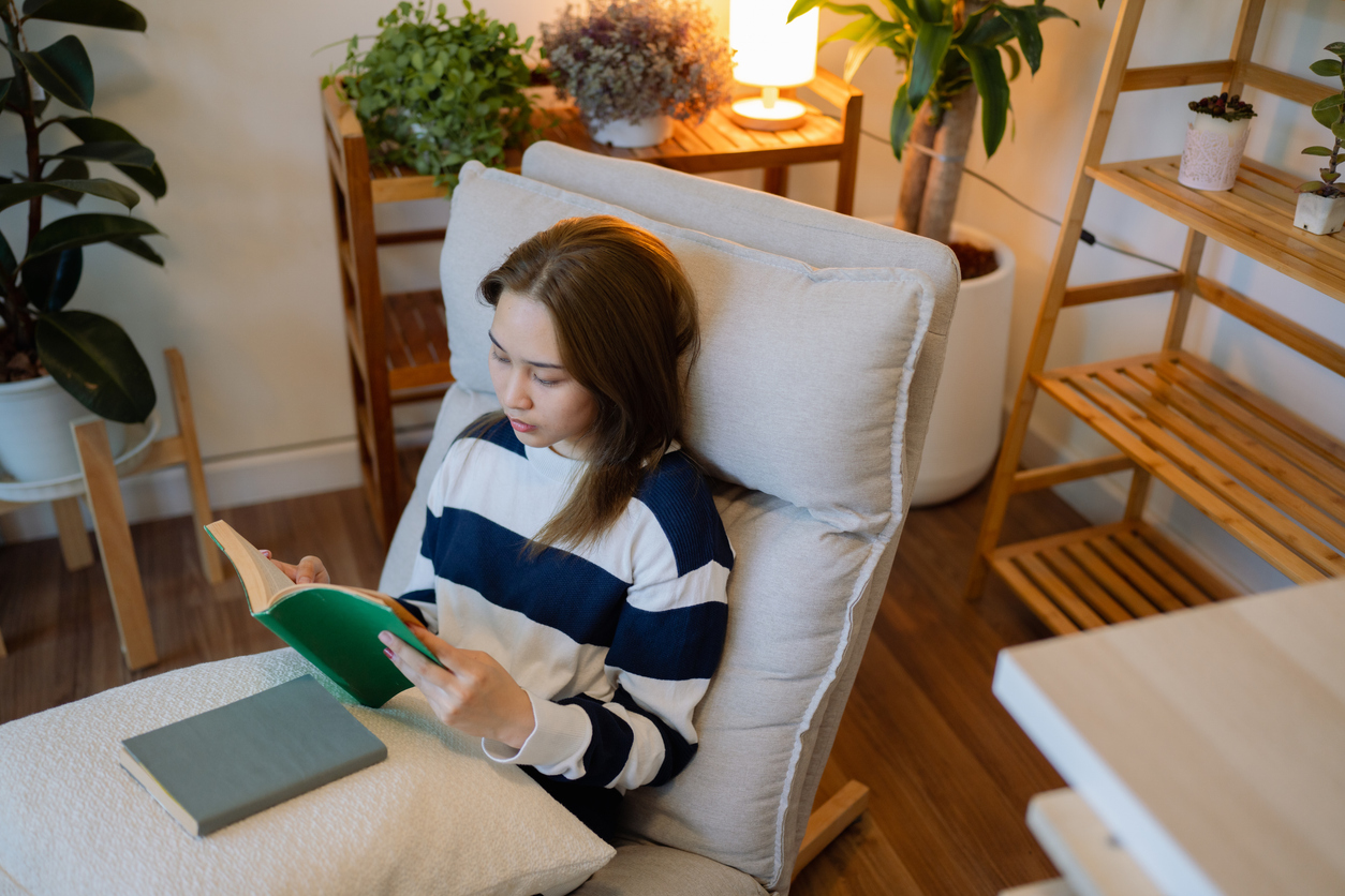 Asian woman reading on the sofa in the evening alone in her living room with the intention and joy of reading.