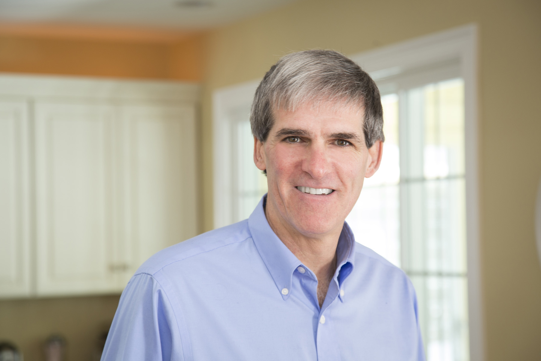 Older man wearing light blue button down shirt smiling in his kitchen