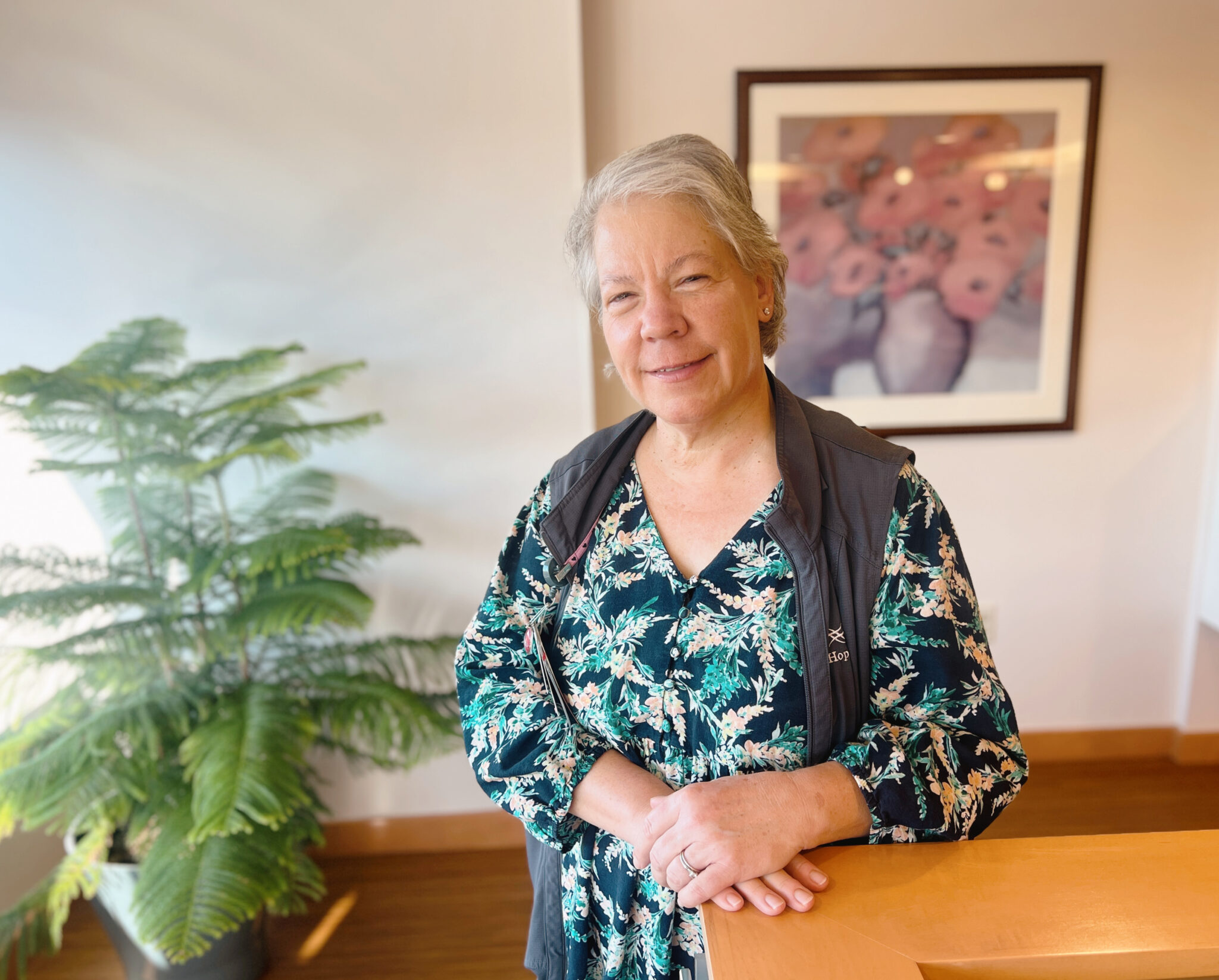 Woman in floral shirt standing in front of a painting, with a tree to the left of her