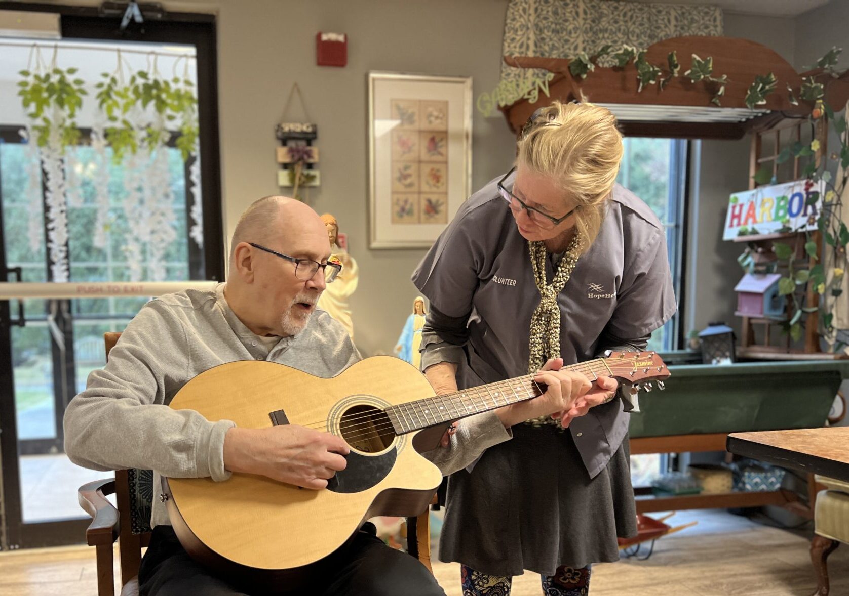 Woman leans over to man who is playing the guitar