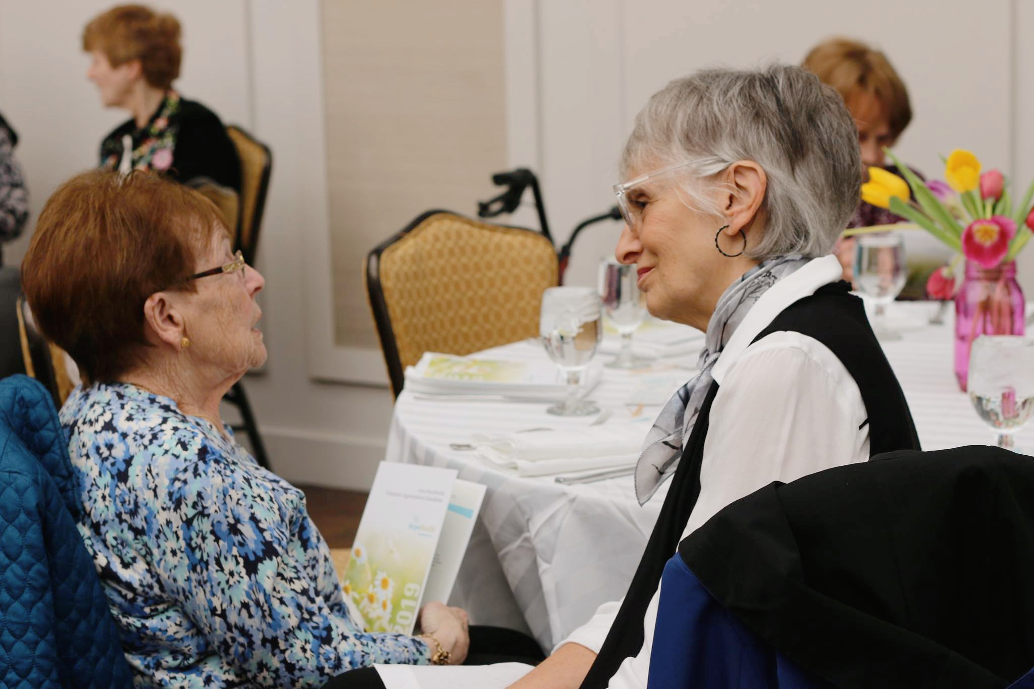 Two older woman sitting at a table speaking compassionately together