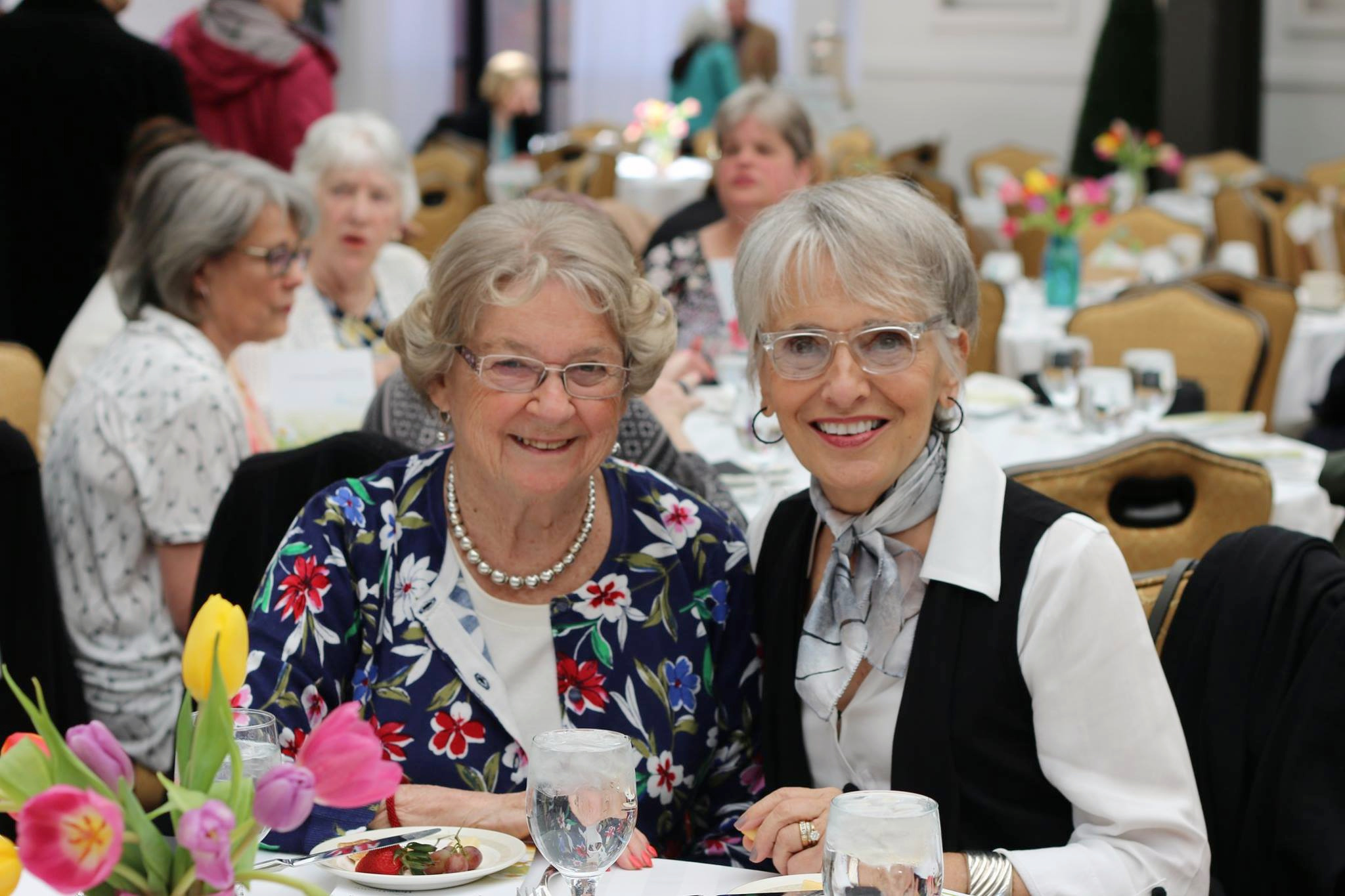 Two older women smiling at a table with colorful tulips