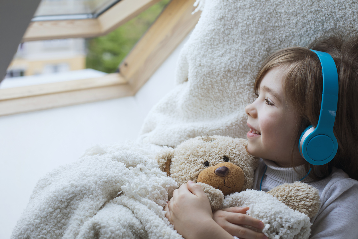 Happy cute boy hugs his teddy bear and listens music at his cozy home.