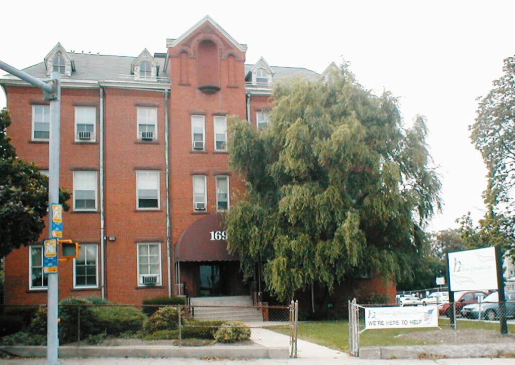Large brick building with a fluffy green tree in front of it.