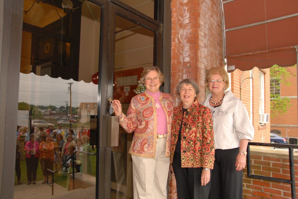 Three older women standing in front of a large glass door.