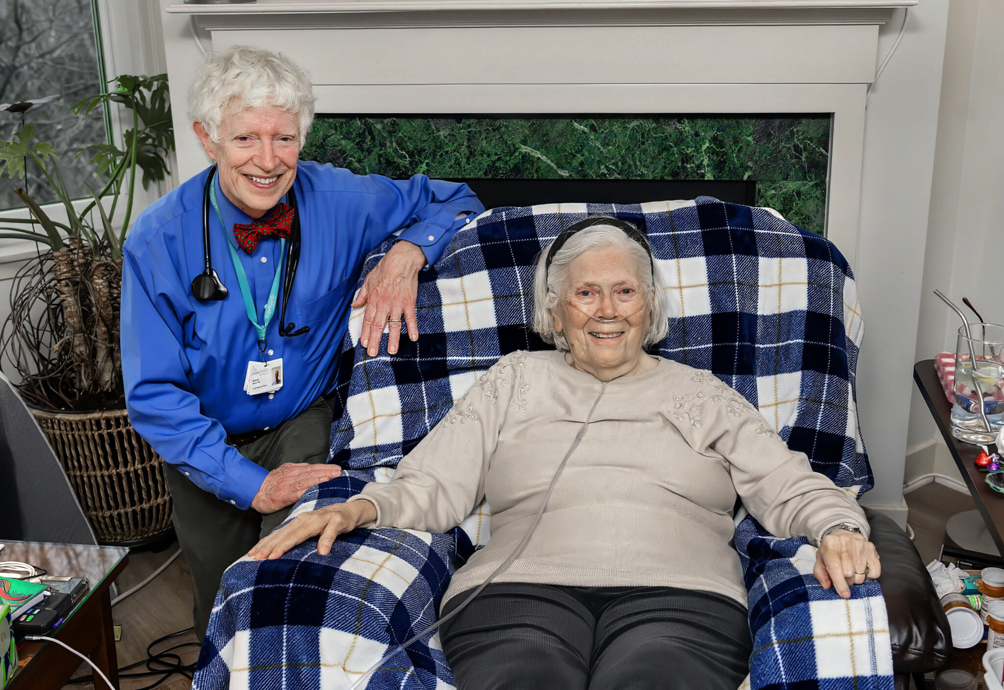 A doctor sits next to a hospice patient sitting in their chair smiling